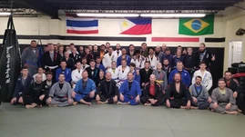 Large group of adults mostly in gis sitting and standing on mats beneath national flags in a gym