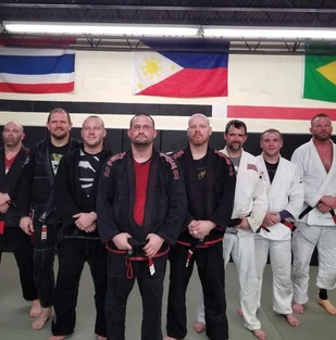 Row of men in jiu-jitsu gis standing on mats beneath wall flags including the Philippines and Brazil
