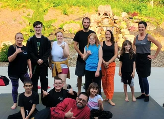 Group of adults and children smiling and posing together on mats outdoors in front of a landscaped rock garden