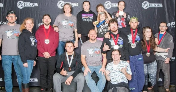 Group of grapplers wearing medals pose together in front of a US Grappling event backdrop