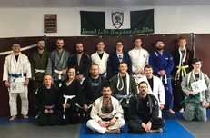 Group of jiu-jitsu students in gis posing on mats under a Round Table Brazilian Jiu-Jitsu banner