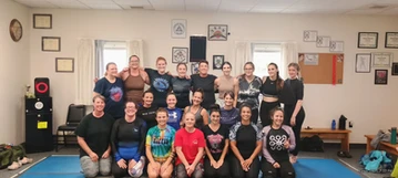 Group of women in athletic clothes pose together on blue mats in a training room