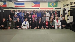 Large group of adults in gis and street clothes posed on the mats beneath national flags on the wall