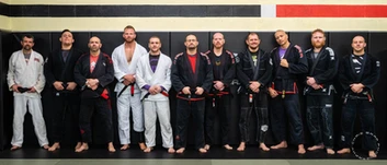 A line of adults in gis and belts standing side by side against a dark gym wall