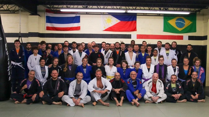 Large group of adults and teens in gis posed in rows on gym mats beneath several national flags